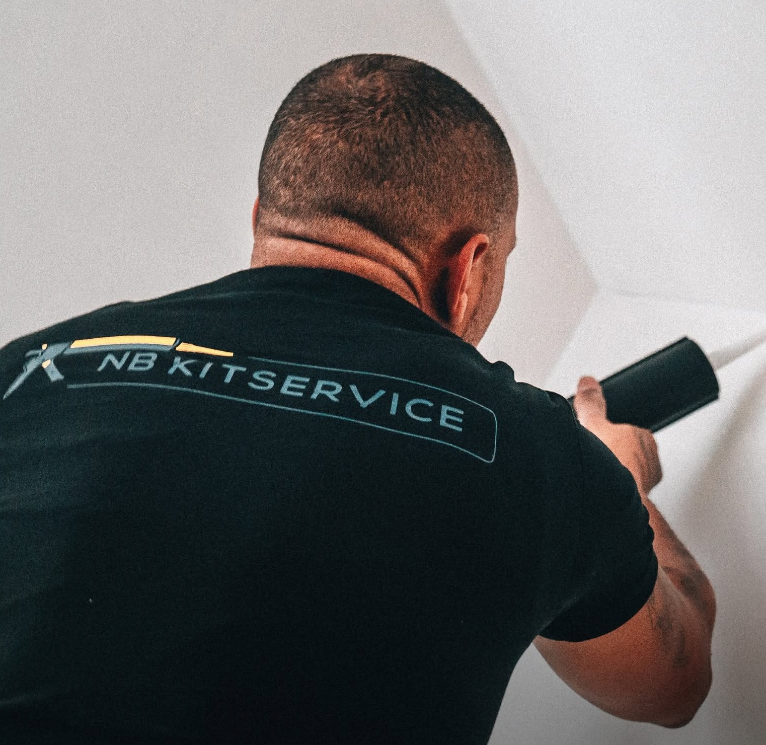 Niek van NB Kitservice, van achteren, kit een hoek tussen wand en plafond af